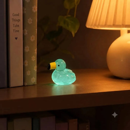 Miniature Glow Swan Assorted (1pc) glowing in a dark setting on a table.