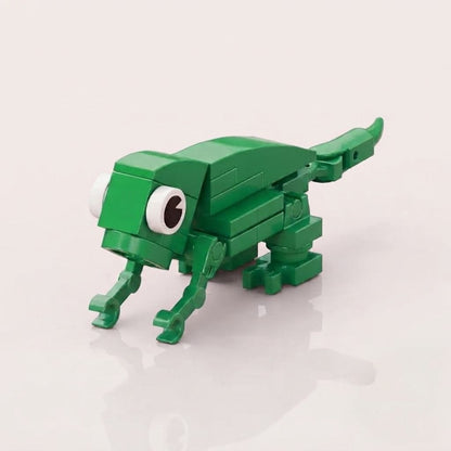 A green toy building-block creature with large white eyes and a long tail, photographed on a clean light background.