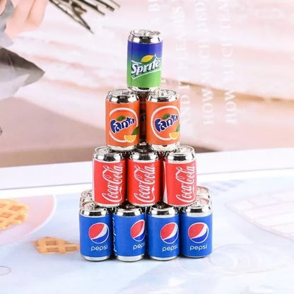 A Miniature Dollhouse Soda Can stacked one upon the other on the floor.