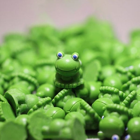A cute Miniature Toy Frog kept on another Miniature Toy Frog with several similar Miniature Toy Frog in the background.