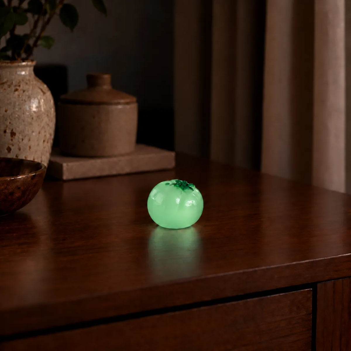 Miniature Glow Tomato Assorted (1pc) glowing on a wooden table in a dimly lit room